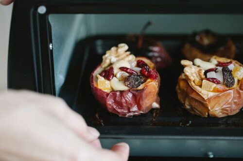 Crop unrecognizable chef removing baking sheet with appetizing stuffed baked apples from electric oven at home